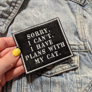 Puede incluir: Parche termoadhesivo negro con texto blanco que dice "Lo siento, no puedo. Tengo planes con mi gato."