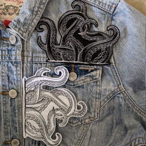 May include: Two black and white embroidered patches of an octopus tentacle design on a blue denim jacket.
