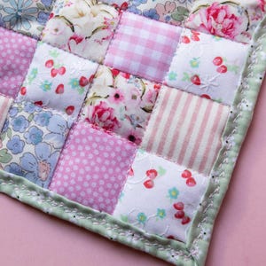 May include: A patchwork quilt with a green border and a variety of floral and patterned fabrics in pink, white, and green.