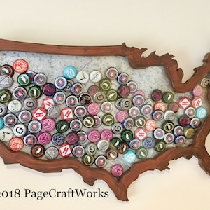 May include: A wooden outline of the United States of America filled with bottle caps of various colours and designs. The wooden frame is a dark reddish brown. The background is a light beige wall. The text "©2018 PageCraftWorks" is in the bottom left corner of the image.