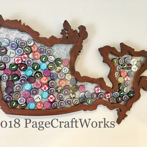 Puede incluir: Un recorte de madera con la forma de Canadá lleno de tapas de botellas. Las tapas de botellas son de varios colores y tienen diferentes logotipos. El texto "©2018 PageCraftWorks" está en la esquina inferior izquierda de la imagen.