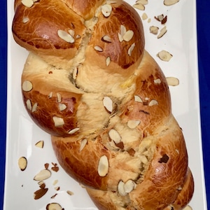 May include: A braided loaf of bread topped with sliced almonds on a white rectangular plate.