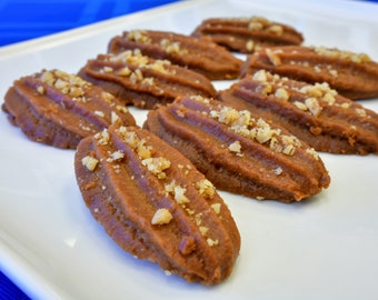May include: A white plate with eight brown, walnut-topped pastries arranged in a row.