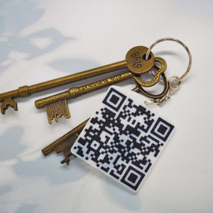 Könnte beinhalten: Ein Satz antiker Schlüssel mit einem silbernen Schlüsselring und einem weißen quadratischen Anhänger mit einem schwarzen QR-Code. Der Anhänger hat auf der Rückseite den Text "Epheser 6:18". Der Schlüsselring hat einen kleinen runden Anhänger mit dem Text "BRB" darauf.