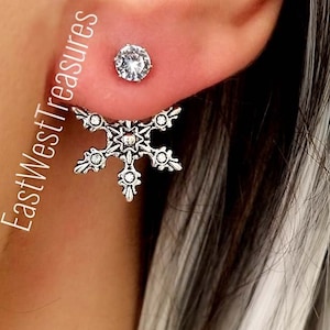 May include: Silver snowflake earrings with clear crystal accents. The snowflake design is detailed and intricate. The earrings are a great way to add a touch of winter magic to any outfit.