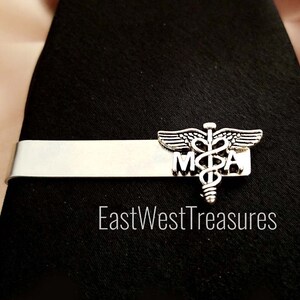May include: Silver tie bar with a medical caduceus symbol and the letters "M.D.A." on a black tie.