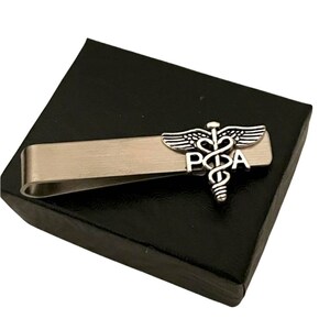 May include: Silver tie clip with a medical caduceus symbol and the letters "PA" on a black background.