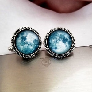 May include: A pair of silver cufflinks with a blue and white moon image in the center of each cufflink.