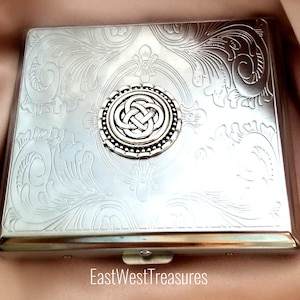 May include: Silver cigarette case with an embossed Celtic knot design. The case has a hinged lid and a silver clasp.