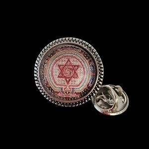 May include: A round, silver-colored lapel pin with a detailed design. The pin features a central image of a red Star of David within a circular pattern of colors. The pin has a textured, beaded edge and a pin back.