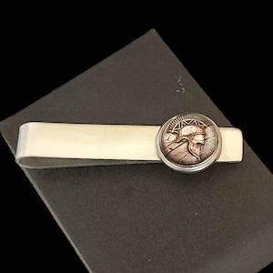 May include: Silver tie bar with a round, copper-toned, detailed design of a Roman soldier's helmet.