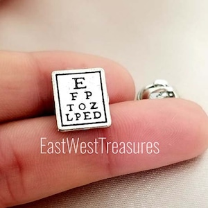 May include: Silver eye chart pin with the letters E, FP, TOZ, and LPED printed on it.