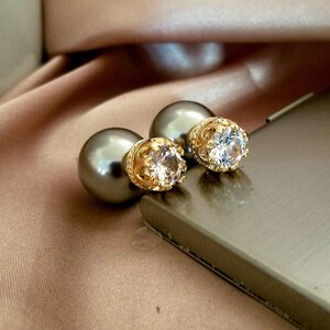 May include: A pair of gray pearl earrings with gold crown accents and clear crystal stones.