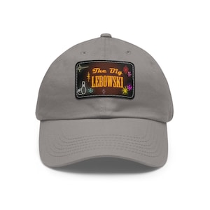 Puede incluir: Gorra de béisbol gris con un parche rectangular con el texto "The Big LEBOWSKI" en un estilo neón retro. El parche incluye gráficos de bolos y estrellas. La gorra tiene una visera curva y una correa de tela.