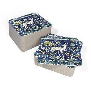 May include: A stack of blue and white ceramic coasters with a floral design and a white deer. The coasters are square and have a raised edge.