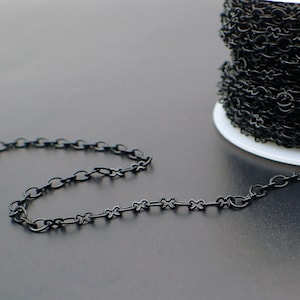 May include: A spool of black chain, with a length of chain lying on a black surface.
