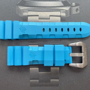 Puede incluir: Correa de reloj azul brillante con hebilla plateada. La correa es de material flexible y tiene agujeros de ajuste. La hebilla est&aacute; grabada con el nombre de la marca. La correa est&aacute; dise&ntilde;ada para un reloj.