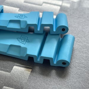 Puede incluir: Primer plano de una correa de reloj azul claro. La correa est&aacute; hecha de un material flexible y presenta una serie de recortes rectangulares y un cierre. La correa tiene el n&uacute;mero "9" y un s&iacute;mbolo de flecha impreso.