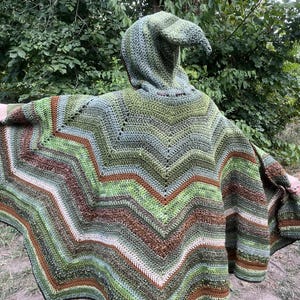 May include: A hooded crochet poncho featuring a multi-colored chevron pattern in various shades of green, brown, and cream. The garment has a pointed hood and a wide, flared silhouette with horizontal stripes of textured yarn throughout the design.