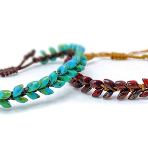 May include: Two beaded bracelets. One is turquoise and green, the other is red and brown. The leaf-shaped beads are strung on a cord. The bracelets have adjustable closures. The background is white.