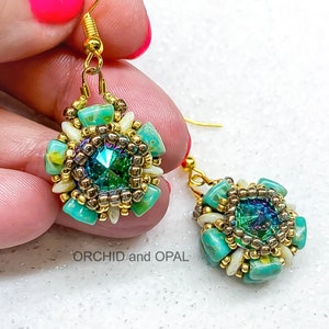 Op de afbeelding: Een paar gouden oorbellen met een ontwerp van turquoise en witte kralen. Elke oorbel heeft een groen, iriserend kristal in het midden.