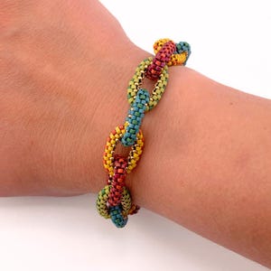 Könnte beinhalten: Ein mehrfarbiges Perlenarmband mit einem Kettenglied-Design. Das Armband hat gelbe, rote, grüne und blaue Perlen. Das Armband wird am Handgelenk getragen.