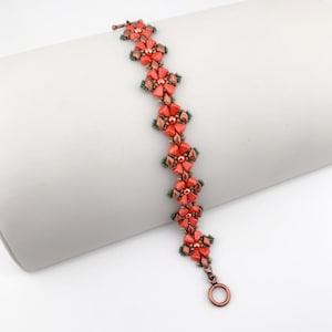 May include: A beaded bracelet featuring a repeating floral pattern made of coral-colored petal-shaped beads and metallic bronze accents. The design includes small dark green seed beads between the floral segments and a circular copper-toned toggle clasp.