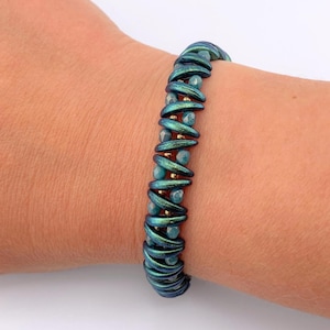 May include: A teal and gold beaded bracelet is worn on a wrist. The bracelet features a series of curved, metallic teal beads, interspersed with smaller, light blue beads and gold accents. The bracelet is a piece of jewelry.