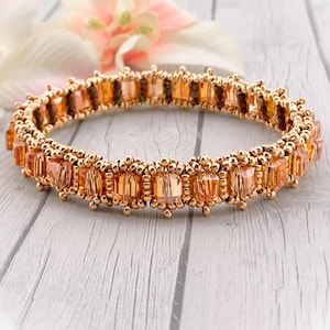 May include: A gold-toned bracelet featuring rectangular orange-colored beads. The bracelet is adorned with smaller, round gold beads between the larger rectangular beads. The design is symmetrical and appears to be handmade, showcasing a blend of elegance and craftsmanship.