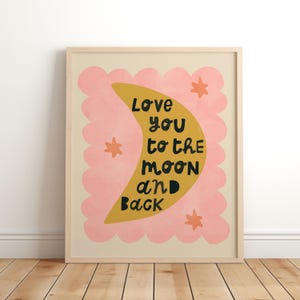 May include: A framed art print with a light wood frame. The artwork features a yellow crescent moon with the words "Love you to the moon and back" in black. The moon is set against a pink scalloped cloud shape, with orange star accents.