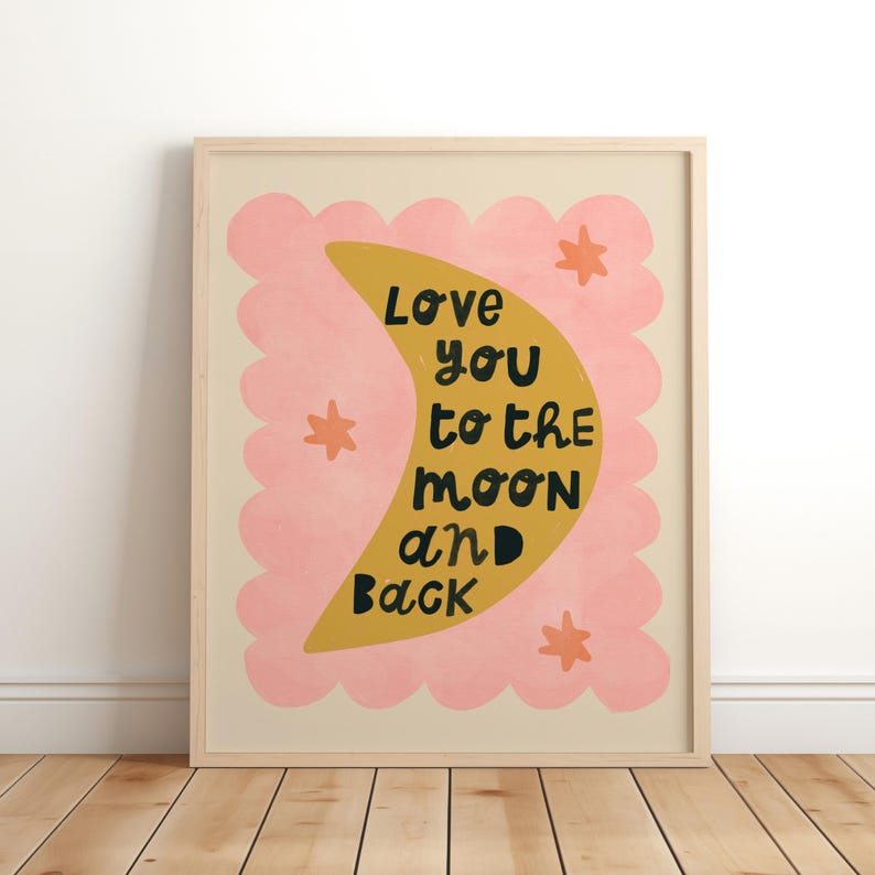 May include: A framed art print with a light wood frame. The artwork features a yellow crescent moon with the words "Love you to the moon and back" in black. The moon is set against a pink scalloped cloud shape, with orange star accents.