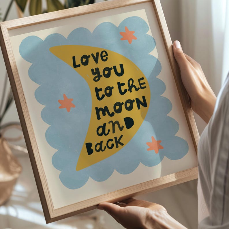 May include: A framed art print with the text "Love you to the moon and back." The artwork features a yellow crescent moon, blue cloud shapes, and orange stars on a cream background. The frame is made of light-colored wood.