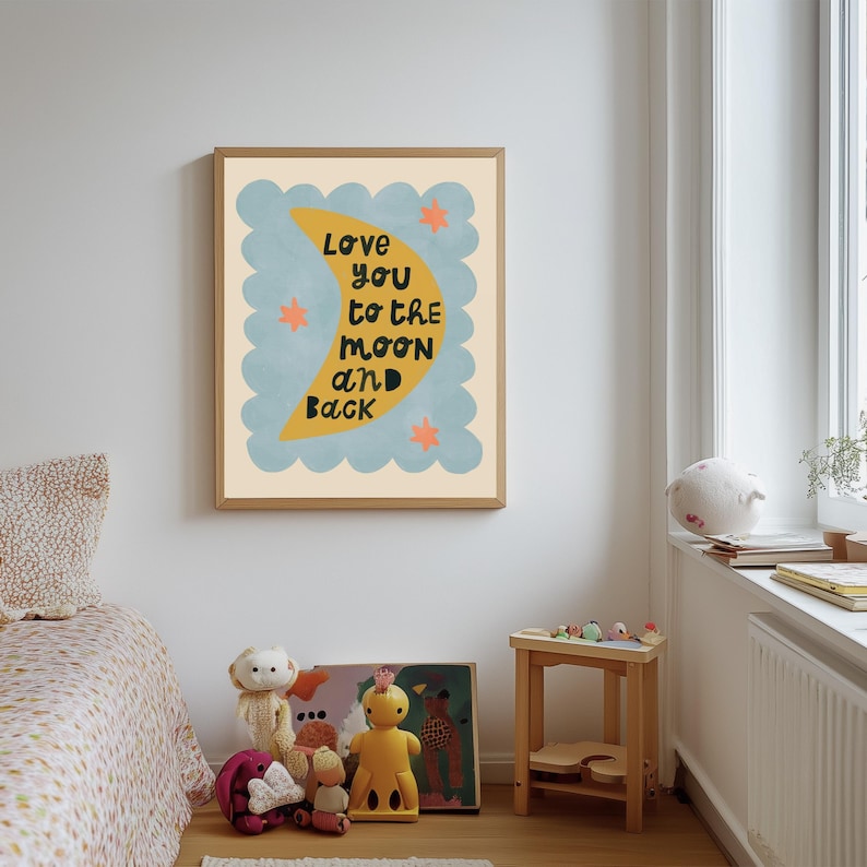 May include: A framed art print with the text "Love you to the moon and back." The artwork features a yellow crescent moon, blue cloud-like shapes, and orange stars on a cream background. The frame is a light brown color.