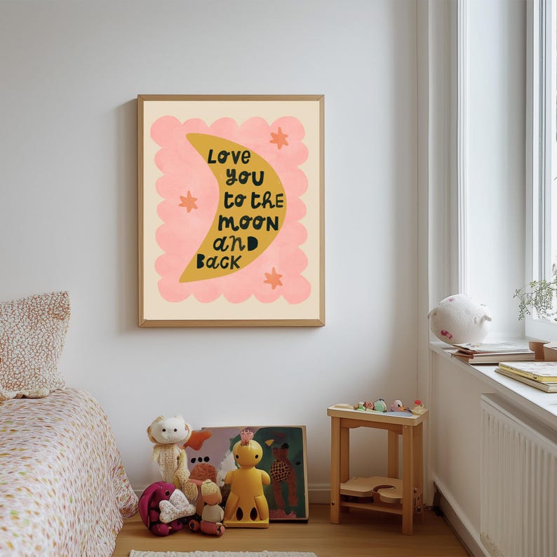 May include: A framed art print with the text "Love you to the moon and back." The artwork features a yellow crescent moon shape with black text, set against a pink scalloped border and cream background. The print is in a child's bedroom.