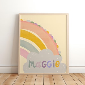 May include: A framed print with a rainbow design and the name "Maggie" in pastel colours. The rainbow arches across the top, with a cloud below. The background is a soft yellow.