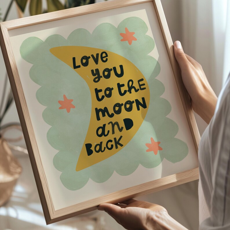 May include: A framed art print with a light wood frame. The artwork features a yellow crescent moon with the words "Love you to the moon and back" in black text. The moon is set against a light green cloud-like shape with orange star accents.