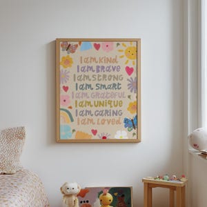 May include: A framed art print with a beige background and colorful illustrations of flowers, butterflies, a rainbow, and a sun. The text reads "I am Kind, Brave, Strong, Smart, Grateful, Unique, Caring, Loved."