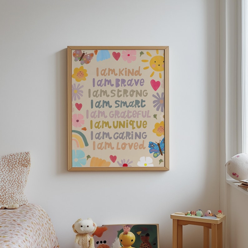 May include: A framed art print with a beige background and colorful illustrations of flowers, butterflies, a rainbow, and a sun. The text reads "I am Kind, Brave, Strong, Smart, Grateful, Unique, Caring, Loved."