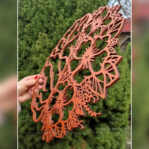 May include: A circular, laser-cut wooden wall art piece featuring an intricate, layered floral design with hibiscus-like flowers and foliage. The wood has a warm, reddish-brown finish, and the cutout pattern creates a delicate, openwork structure.