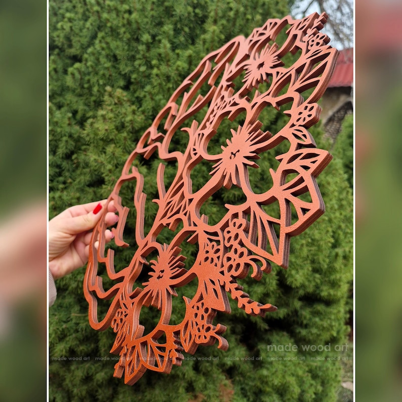 May include: A circular, laser-cut wooden wall art piece featuring an intricate, layered floral design with hibiscus-like flowers and foliage. The wood has a warm, reddish-brown finish, and the cutout pattern creates a delicate, openwork structure.