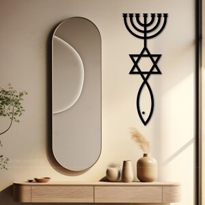 May include: A black wooden wall art piece featuring a menorah, Star of David, and fish symbol. A large oval mirror with a gold frame is on the left. A wooden console table with decorative vases and bowls is below.
