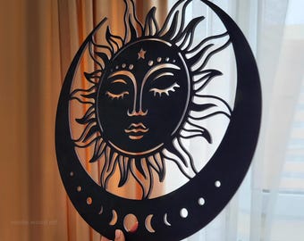 Puede incluir: Arte de pared de madera negra con un diseño celestial de un sol y una luna creciente. El sol tiene una cara con los ojos cerrados y la luna muestra fases. El texto "made wood art" es visible en la parte inferior izquierda.