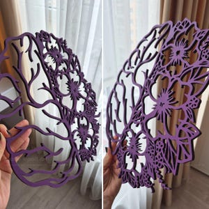May include: A purple laser-cut wooden wall art piece shaped like a human brain. One half of the brain features intricate, branching neural-like patterns, while the other half is composed of detailed floral cutouts with various flower shapes.