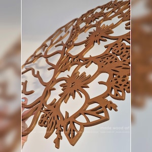 May include: A circular brown wooden wall art piece featuring an intricate laser-cut design of a tree with stylized branches, leaves, and floral elements. The surface has a smooth, matte finish, and the text made wood art is visible in the corner.