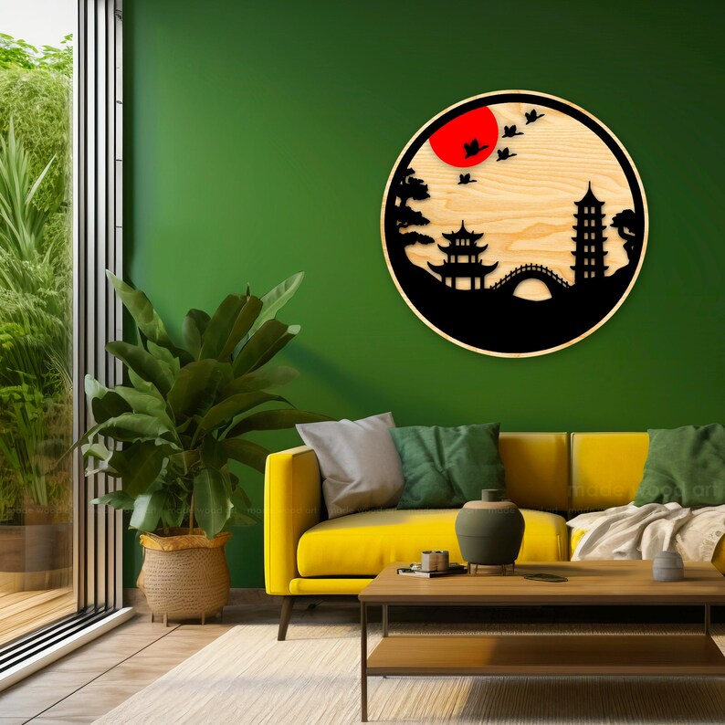 May include: A wooden wall decor featuring a black silhouette of a Japanese landscape with a pagoda, bridge, trees, and a red sun. The decor is circular and mounted on a green wall in a living room setting.