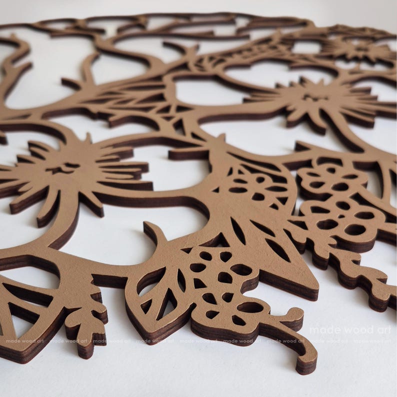May include: A circular brown wooden wall art piece featuring an intricate laser-cut design of stylized flowers, leaves, and branches. The layered wood construction creates a dimensional effect with cutouts throughout the floral pattern.