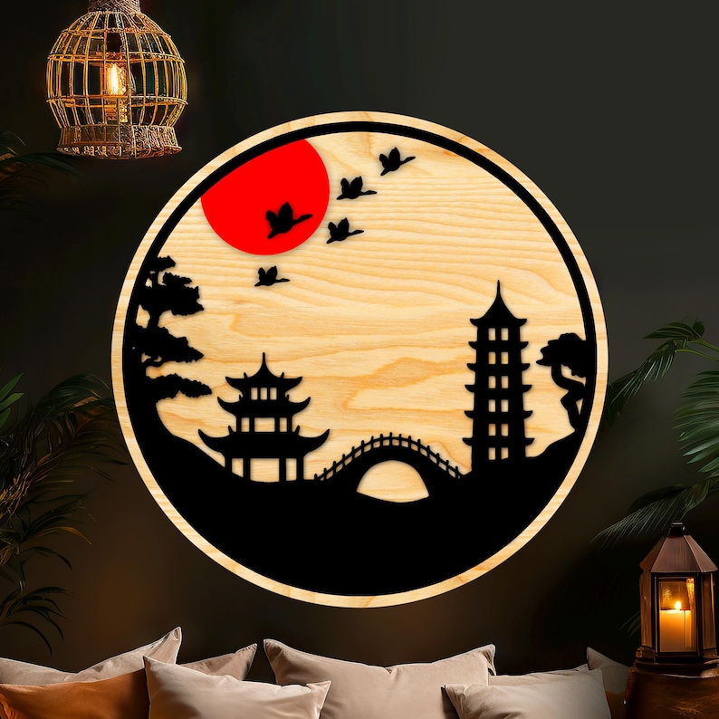 May include: A round wooden wall decor with a black silhouette of a Japanese garden scene. The scene includes a pagoda, a bridge, trees, and birds flying in a red sun.