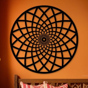 May include: A black, circular wooden wall art piece with a geometric, radial design. The artwork is mounted on an orange wall, and the design features a series of intersecting curved lines that create a spiral pattern. The piece is a decorative element.