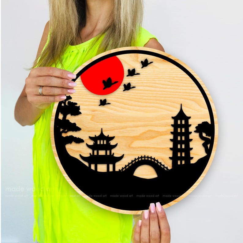 May include: A round wooden wall art piece with a black silhouette of a Japanese pagoda, bridge, and trees against a red sun and a light wood background.