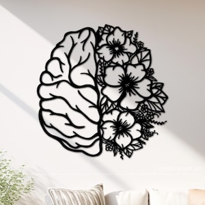 May include: A black wall art piece featuring a split design. The left side depicts the anatomical structure of a human brain with distinct lobes and folds, while the right side is composed of detailed floral arrangements with leaves and petals.